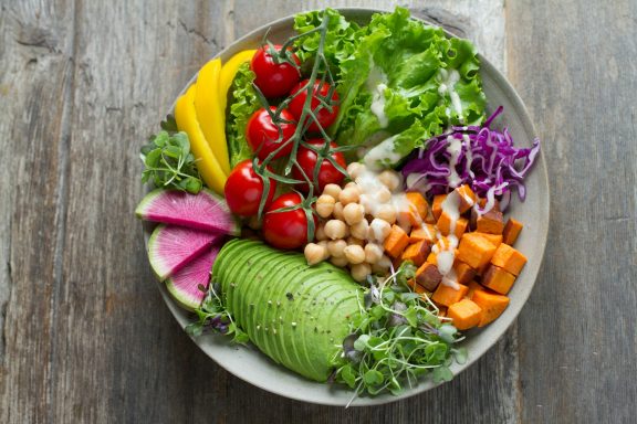 Bunte Saladplatte mit Avocado, Süßkartoffeln, Tomaten, Mangos, und verschiedenen Blattsalaten.